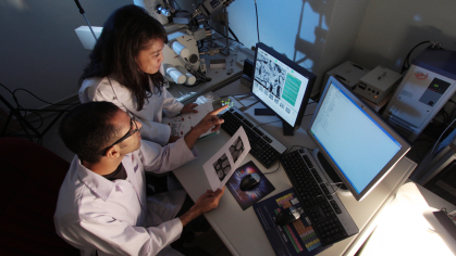Two biomedical researchers standing next to each other looking at data and monitor