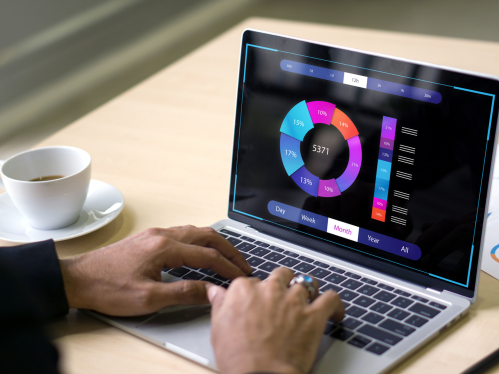 Hands typing laptop keyboard. Laptop screen shows circular graph