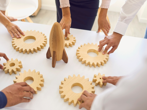 Hands of five people holding cogs surrounding a rocket, as a sign of innovation and research